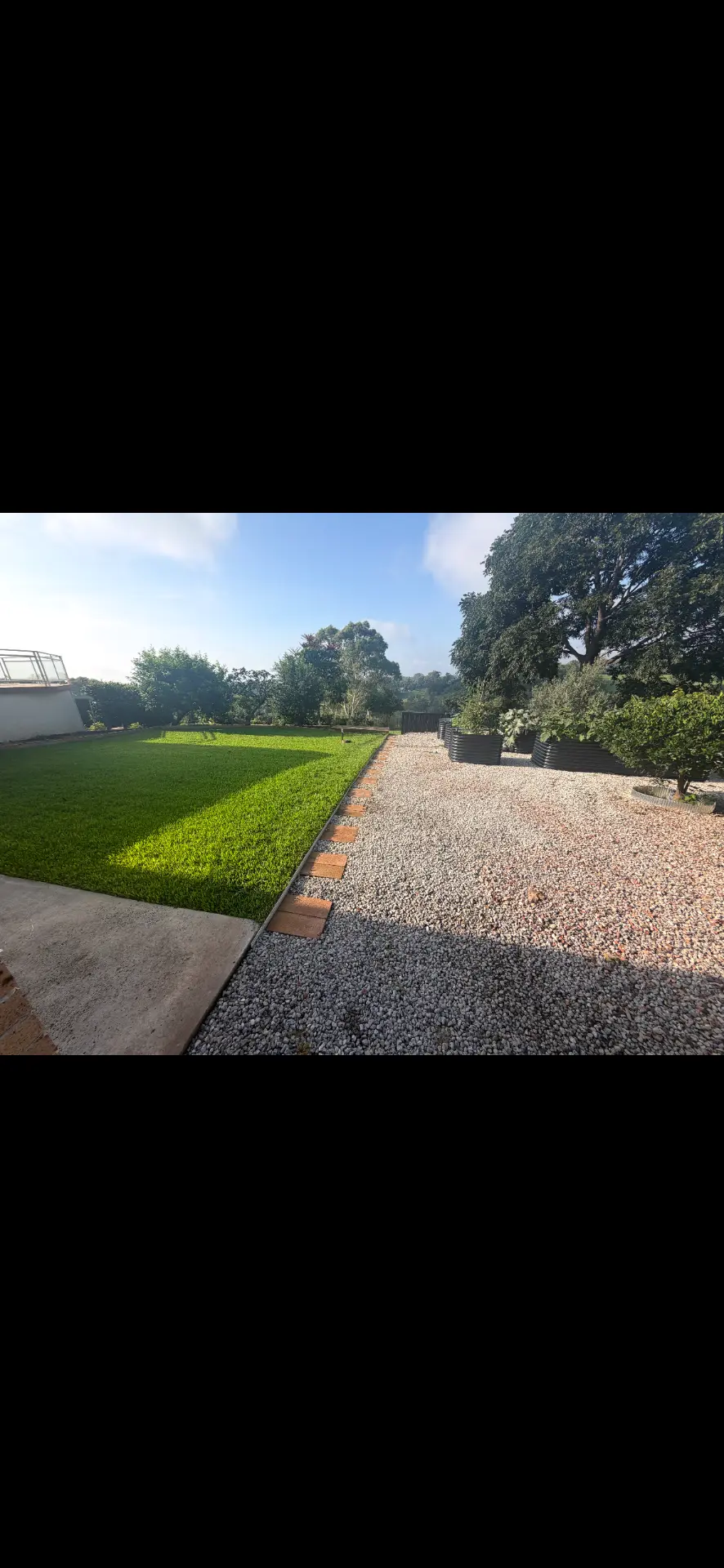 Manicured lawn with brick edging beside a new white gravel bed and raised planters